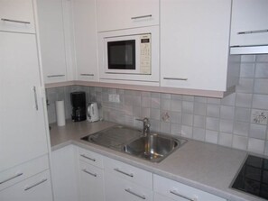 A kitchen with white cabinets, a stainless steel sink, a microwave, and a coffee maker. - Valère Leukerbad # 2-bed apartment, Dusche, WC by Interhome (Leukerbad)