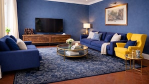 Un salon avec un canapé bleu, un fauteuil jaune, une table basse et un téléviseur à écran plat.