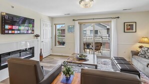 Sala de estar con televisor, sofá, mesa de centro y vista a un jardín.