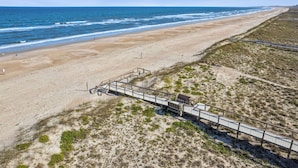 Ein Strand mit einer Holzpromenade, die zu einer Struktur führt, feinem Sand und dem Meer.