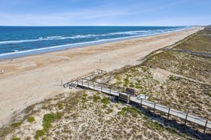 Ein Strand mit einer Holzpromenade, die zu einer Struktur führt, feinem Sand und dem Meer.