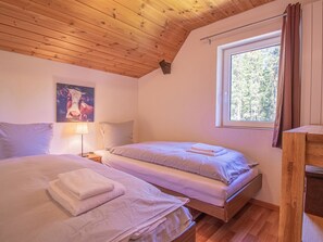 Ein Schlafzimmer mit zwei Betten, einem Fenster mit Vorhängen, einer Holzbalkendecke und einem Bild an der Wand.