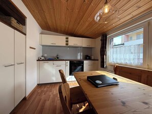Cocina compacta con armarios blancos, una mesa de madera y una lámpara colgante.