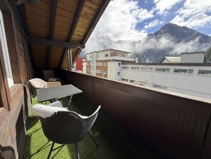 En balkon med udsigt til bjerge, et bord og to stole.