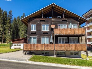 Ein mehrstöckiges Holzhaus mit Balkonen, einer Schotterauffahrt und einem bewaldeten Hintergrund.