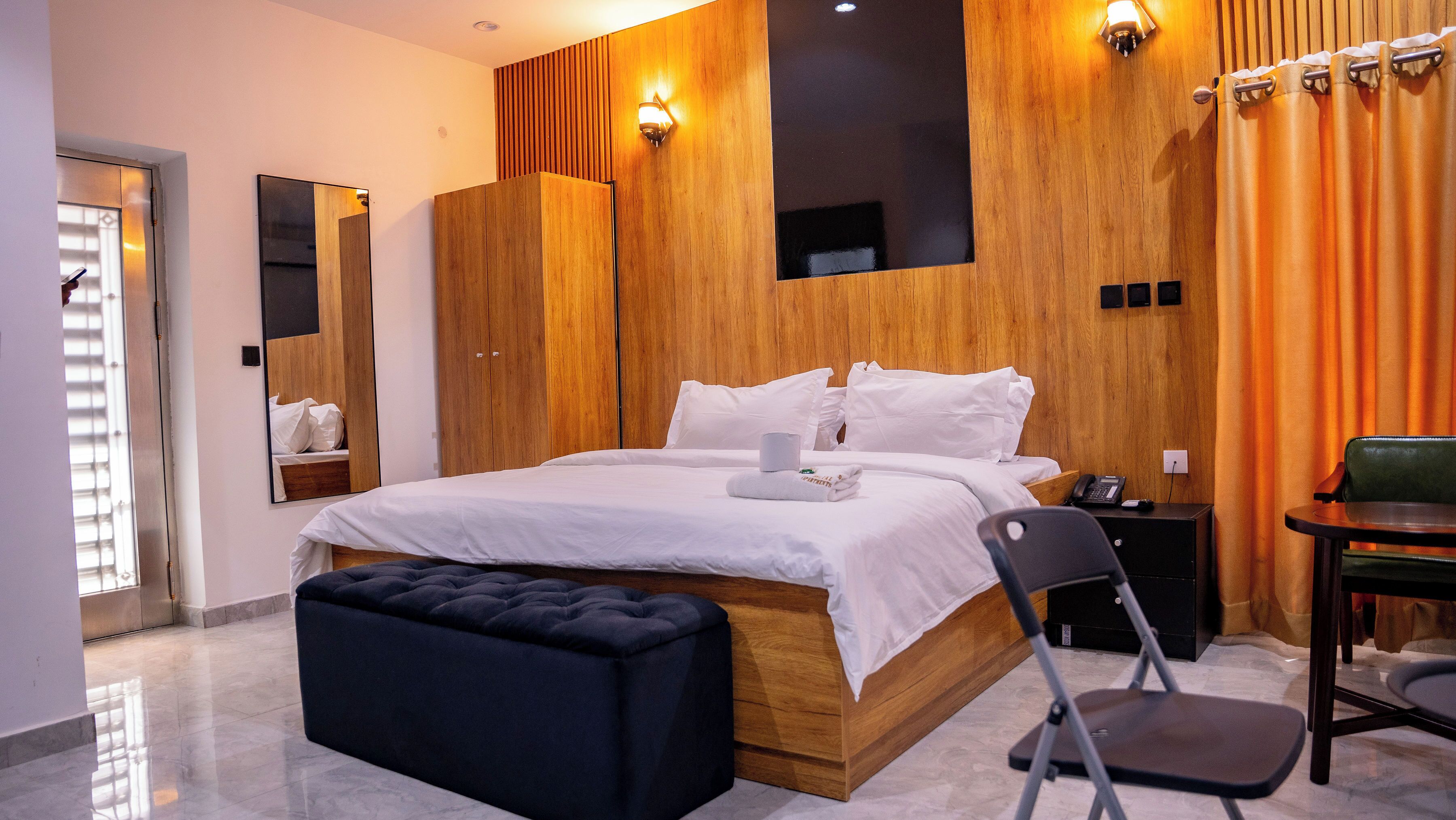 Ein modernes Hotelzimmer mit einem großen Bett, einem Holzkopfteil, einem Schreibtisch mit Stuhl und einem Badezimmer mit Spiegel und Toilette.