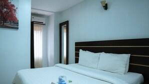 Una habitación de hotel con cama, ventana con cortinas, aire acondicionado de pared y un cuadro.