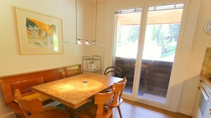 Ein Essbereich mit Holztisch und -stühlen, einer Bank, einem gerahmten Bild an der Wand und einer Glastür zum Außenbereich.