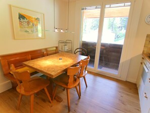 A dining area with a wooden table and chairs, a bench, a framed picture on the wall, and a sliding glass door leading to an outdoor area. - Furkablick Alice by Arosa Holiday Appartement/Fewo,   Furkablick Alice by Interhome (Arosa)
