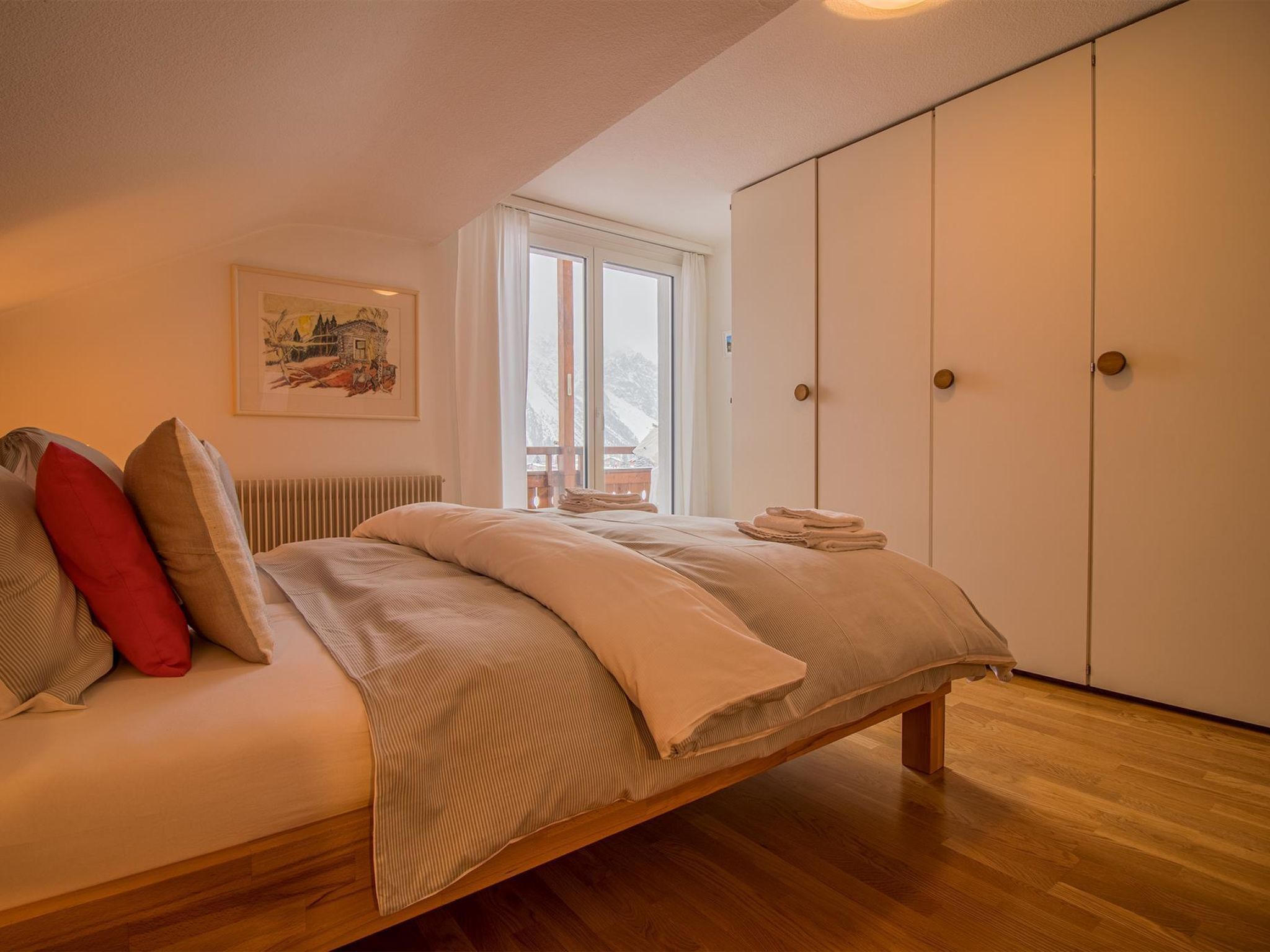 Un dormitorio con cama, radiador, ventana con cortinas, un cuadro en la pared y armario.