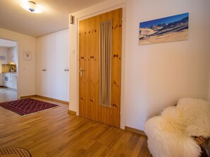 A room with a wooden door, a red patterned rug, and a white furry object. - Furkablick Alice by Arosa Holiday Appartement/Fewo,   Furkablick Alice by Interhome (Arosa)