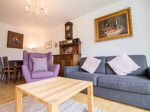 A living room with a wooden coffee table, a purple armchair, a grey sofa, a wooden cabinet, and a wall-mounted clock. - Casa Viktoria A37 by Arosa Holiday Appartement/Fewo, Dusche, WC, 4-Bettwohnung by Interhome (Arosa)
