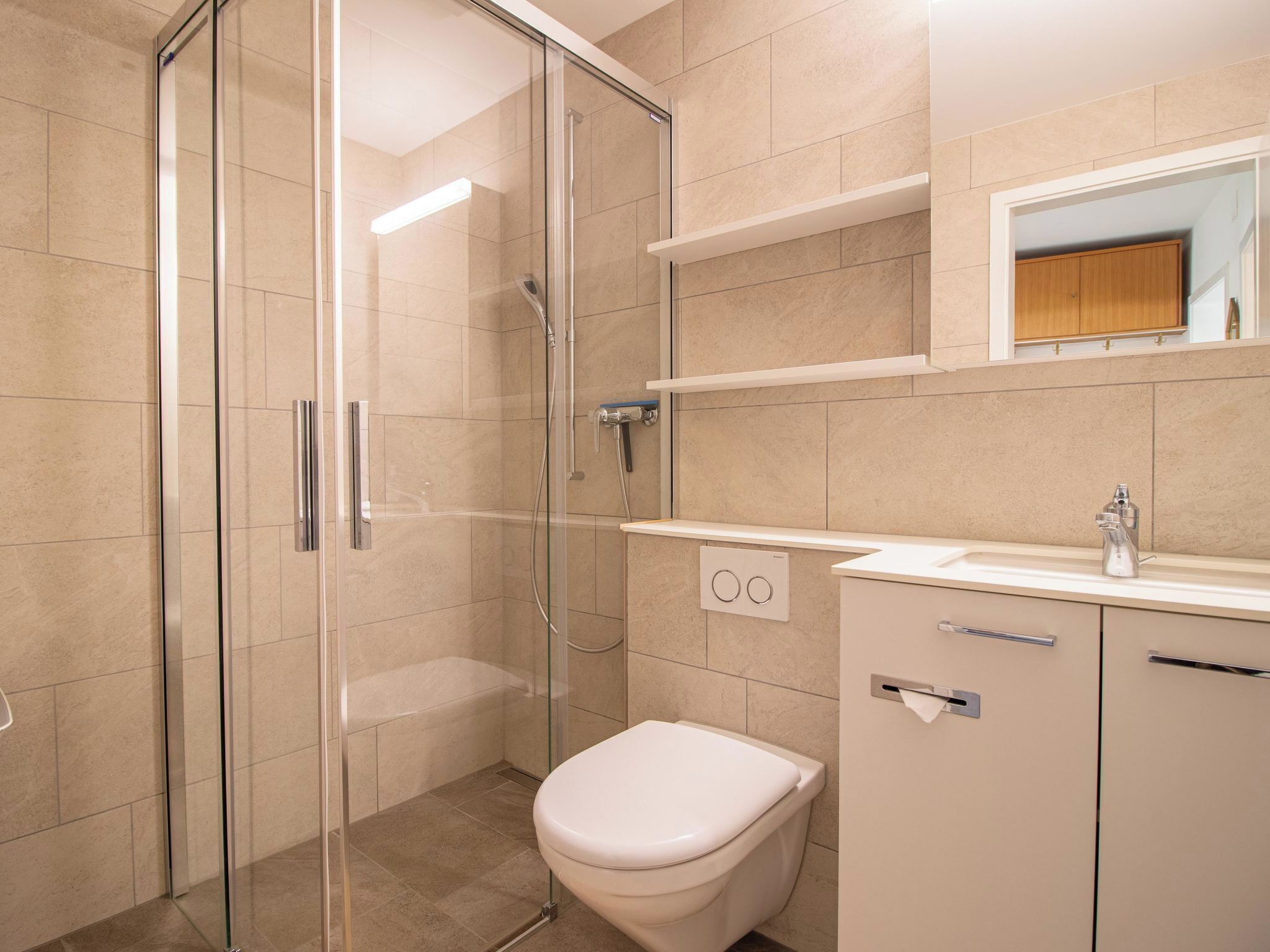 A modern bathroom with a glass-enclosed shower, a toilet, and a sink with a mirror above.