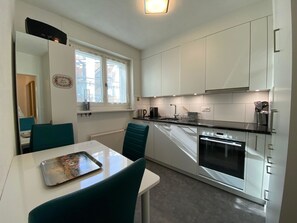 A modern kitchen with white cabinets, a built-in oven, and a dining area with a table and chairs. - Casa Viktoria A37 by Arosa Holiday Appartement/Fewo, Dusche, WC, 4-Bettwohnung by Interhome (Arosa)