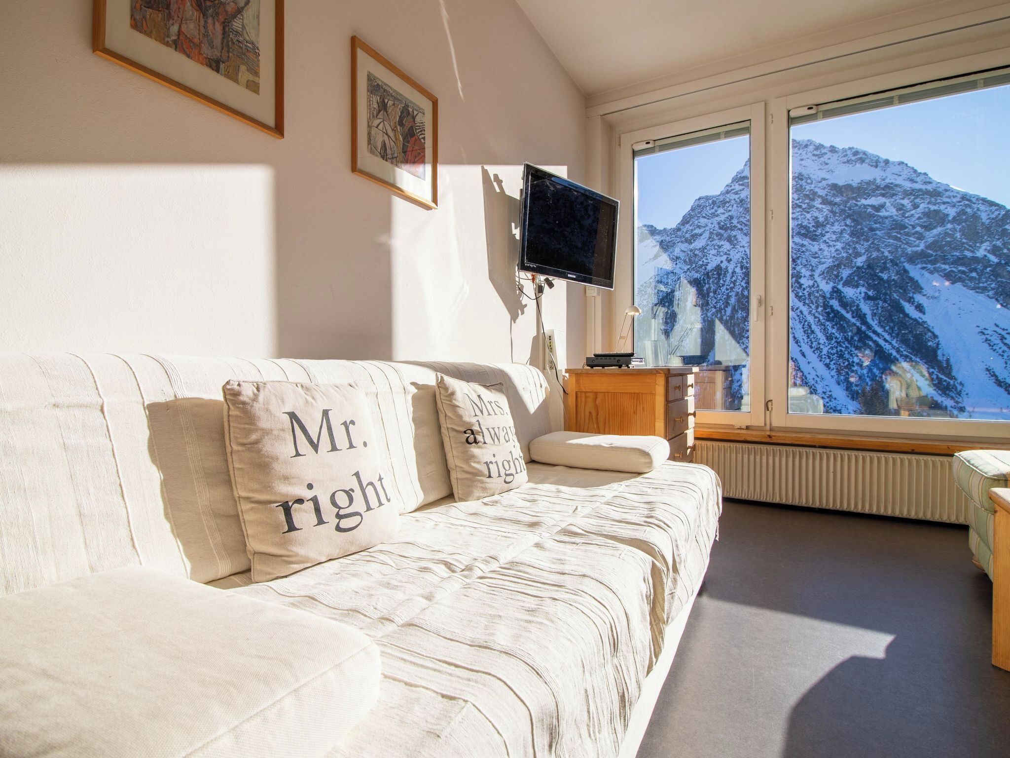 Ein gemütliches Wohnzimmer mit einer Couch, einem flachbildfernseher an der Wand und einem großen Fenster mit Blick auf die Berge.