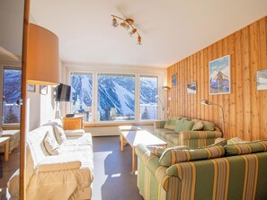 A cozy living room with a sofa, a coffee table, and a TV. There are large windows with a view of snowy mountains. - Casa Viktoria B43 by Arosa Holiday Appartement/Fewo,  , 6-Bettwohnung by Interhome (Arosa)