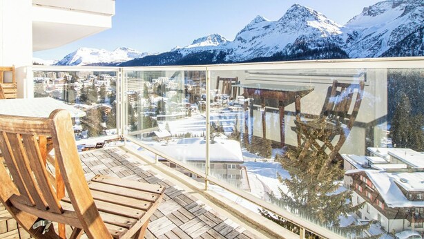 Een houten terras met een glazen balustrade met uitzicht op een besneeuwd berglandschap.