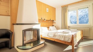 Een slaapkamer met een bed, een openhaard, een stoel en een raam met uitzicht op besneeuwde bergen.
