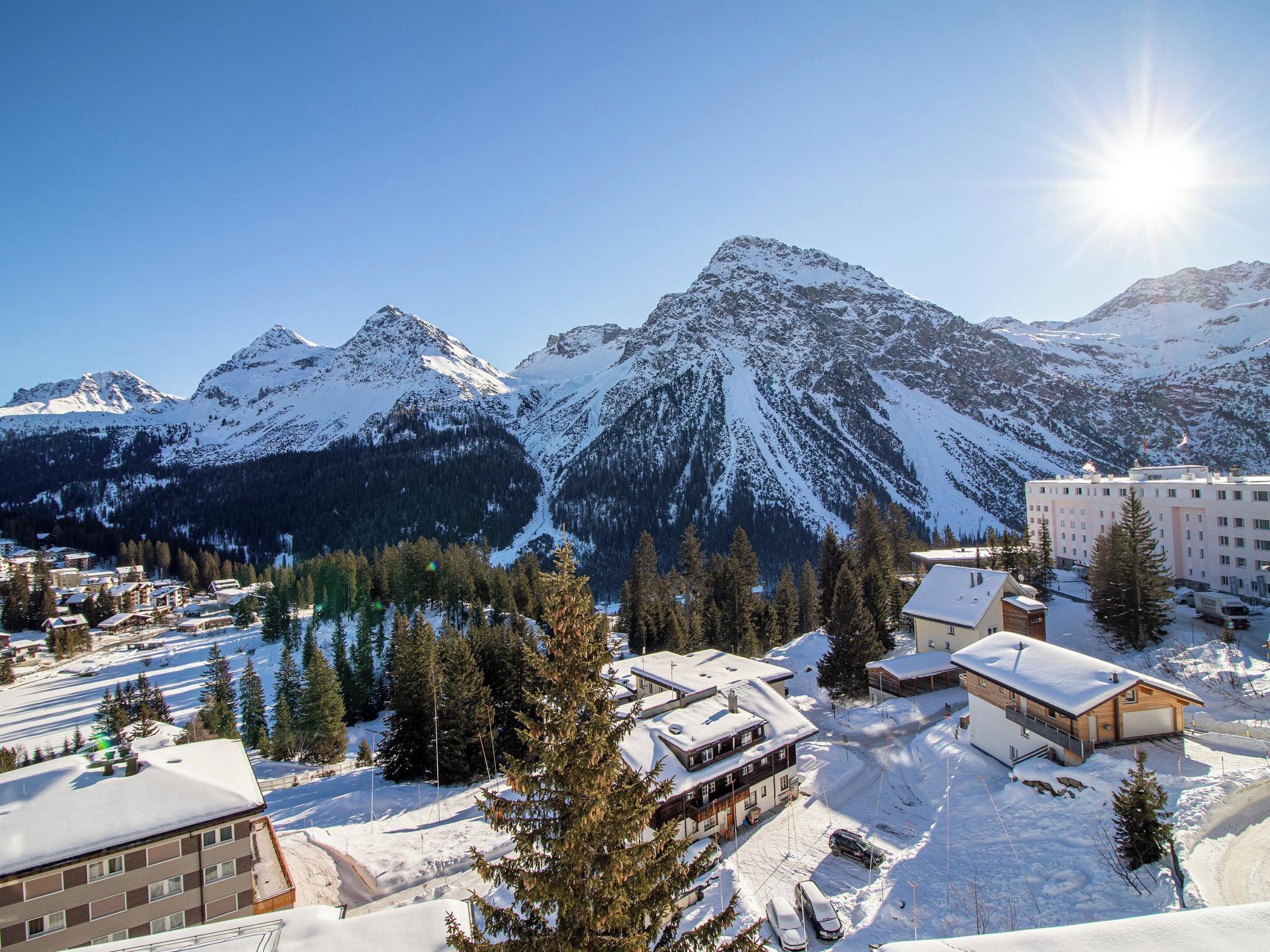 Une station de montagne avec des sommets enneigés, un lac et des bâtiments aux toits couverts de neige.
