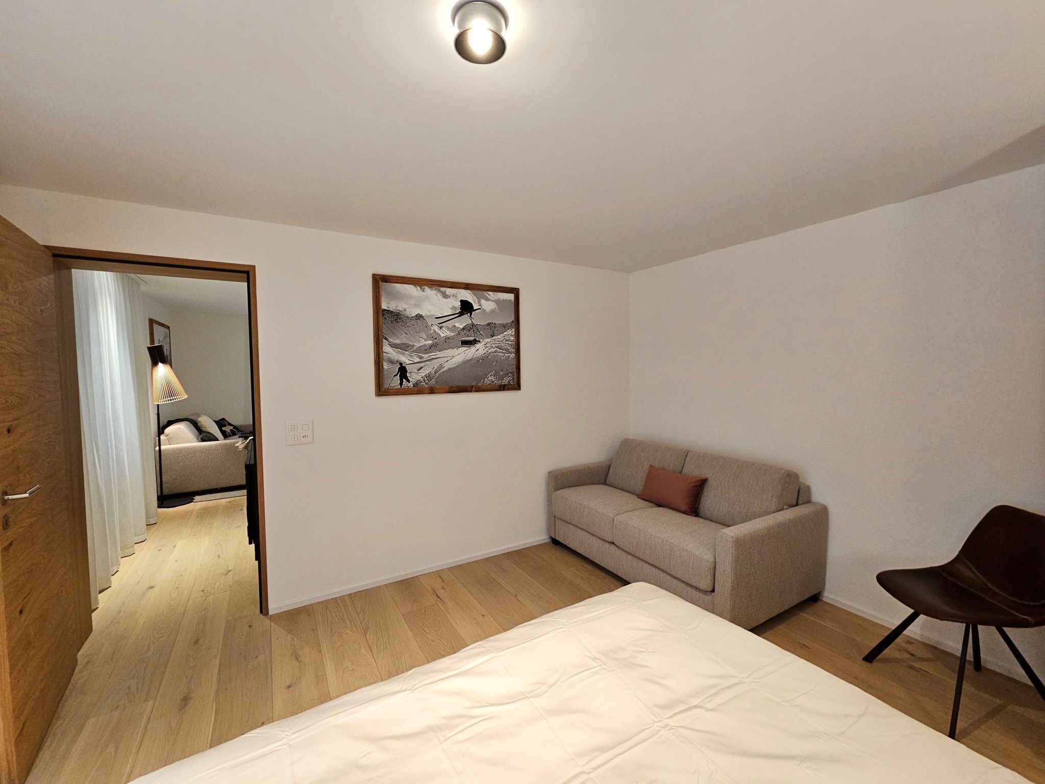 A bedroom with a bed, a sofa, a chair, a painting, and a wooden floor.