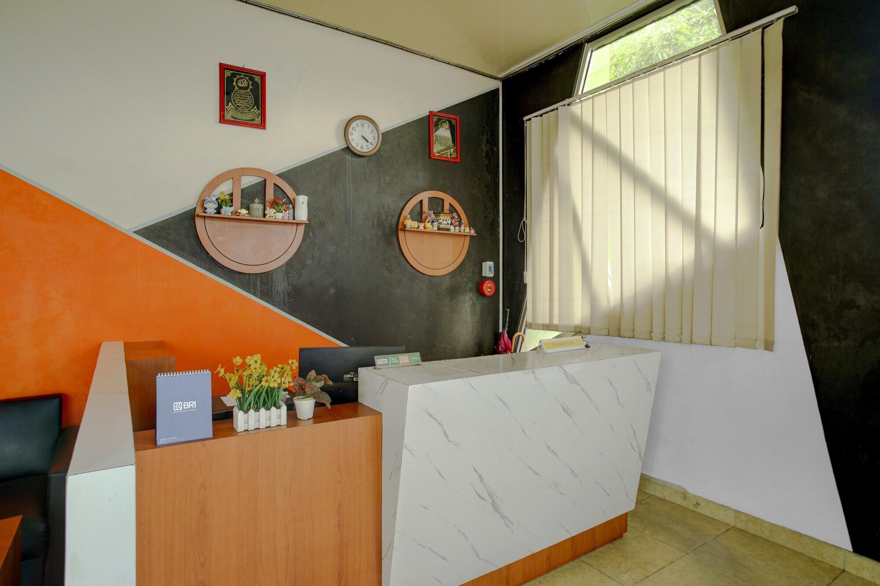 A reception desk with a white marble top, two wooden shelves with decorative items, a clock, and a window with blinds.