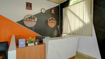 A reception desk with a marble top, two wooden shelves with decorative items, a clock, and a window with blinds.