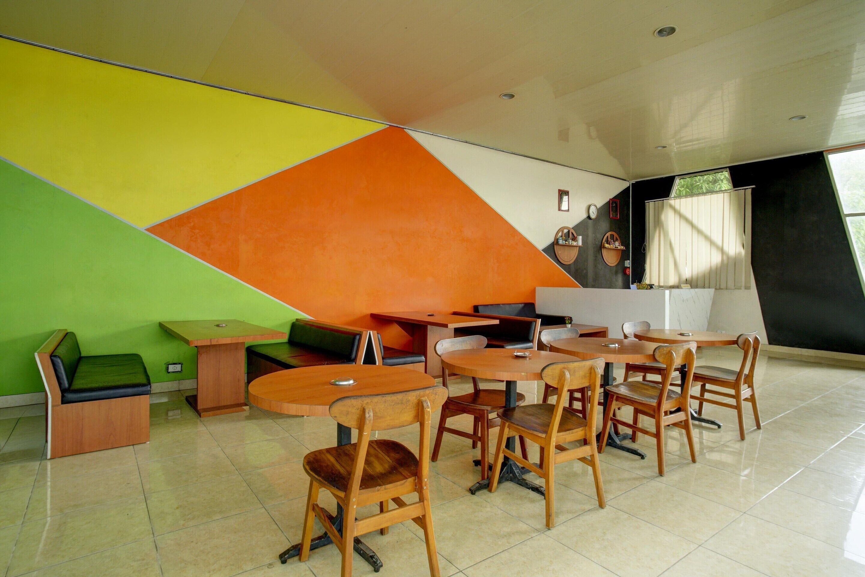 A modern interior with a dining area featuring wooden tables and chairs, a green sofa, and a colorful geometric wall design.