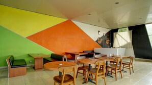 A modern interior with a dining area featuring wooden tables and chairs, a green sofa, and a colorful geometric wall design. - Lima Residence Deluxe Twin (Bandar Lampung)