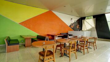 A modern interior with a dining area featuring wooden tables and chairs, a green sofa, and a colorful geometric wall design.
