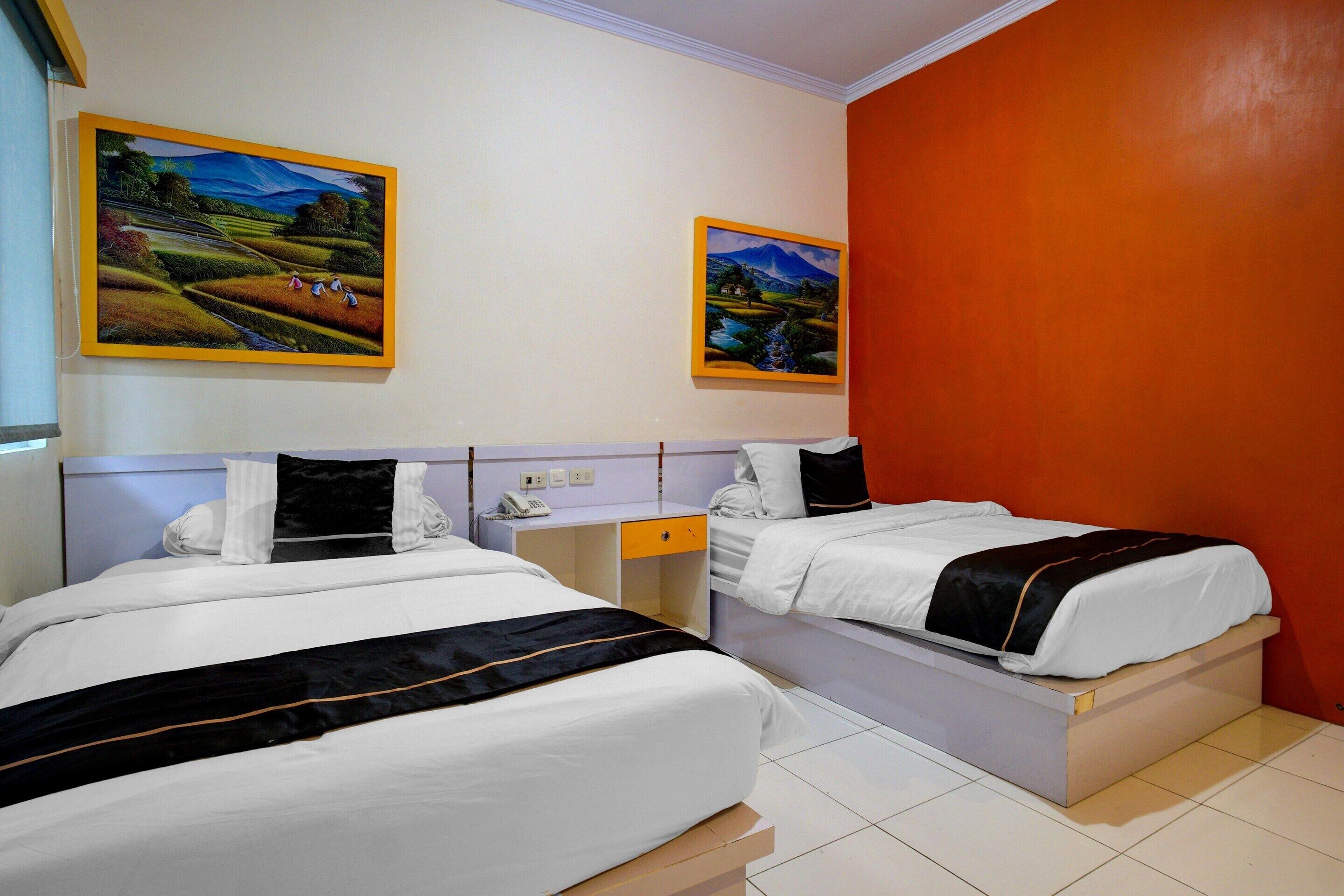 A hotel room with two beds, a desk, and two paintings on the wall.