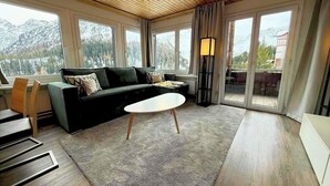 A modern living room with a sofa, a coffee table, and a view of mountains through large windows. - Miraflor Anita by Arosa Holiday Appartement/Fewo, Bad, WC, 6-Bettwohnung by Interhome (Arosa)