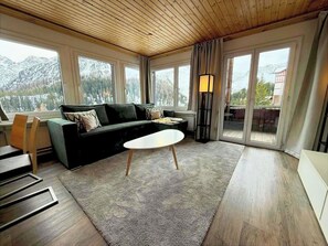 A modern living room with a sofa, a coffee table, and a view of mountains through large windows. - Miraflor Anita by Arosa Holiday Appartement/Fewo, Bad, WC, 6-Bettwohnung by Interhome (Arosa)