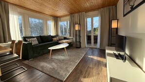 A modern living room with a wooden ceiling, a green sofa, a white coffee table, and a TV on a white stand. - Miraflor Anita by Arosa Holiday Appartement/Fewo, Bad, WC, 6-Bettwohnung by Interhome (Arosa)