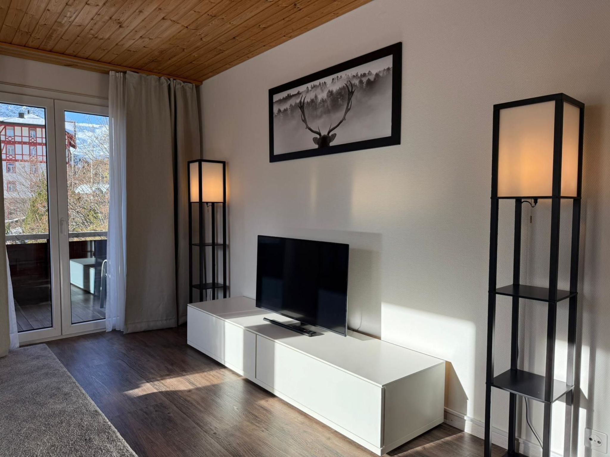 Una sala moderna con un televisor de pantalla plana, un mueble blanco y dos lámparas de pie.