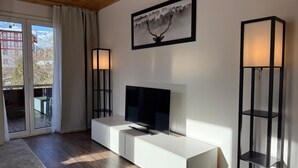 A modern living room with a flat-screen TV, a white cabinet, and two floor lamps. - Miraflor Anita by Arosa Holiday Appartement/Fewo, Bad, WC, 6-Bettwohnung by Interhome (Arosa)