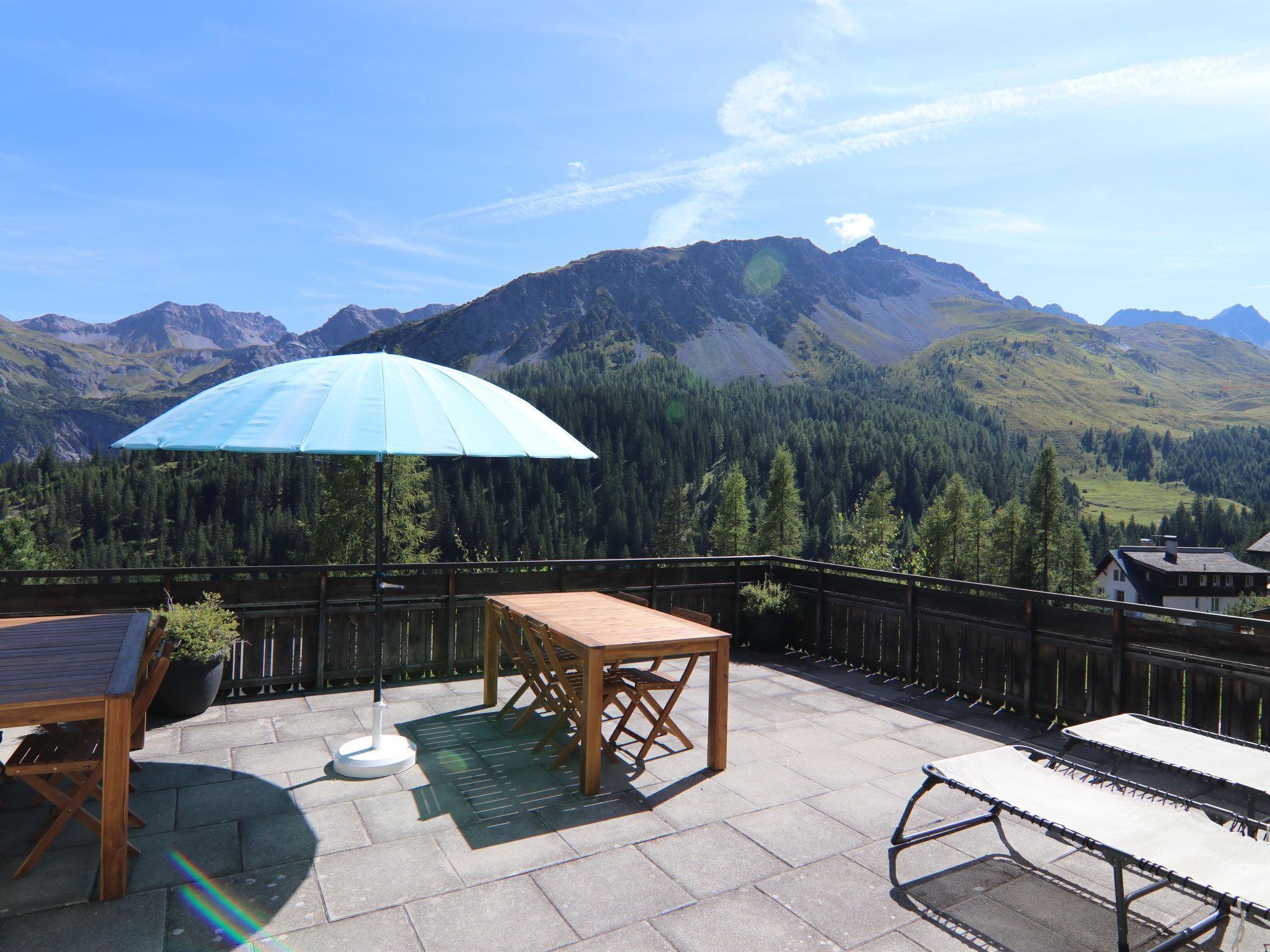 Eine Terrasse im Freien mit Tisch, Stühlen und einem blauen Sonnenschirm.