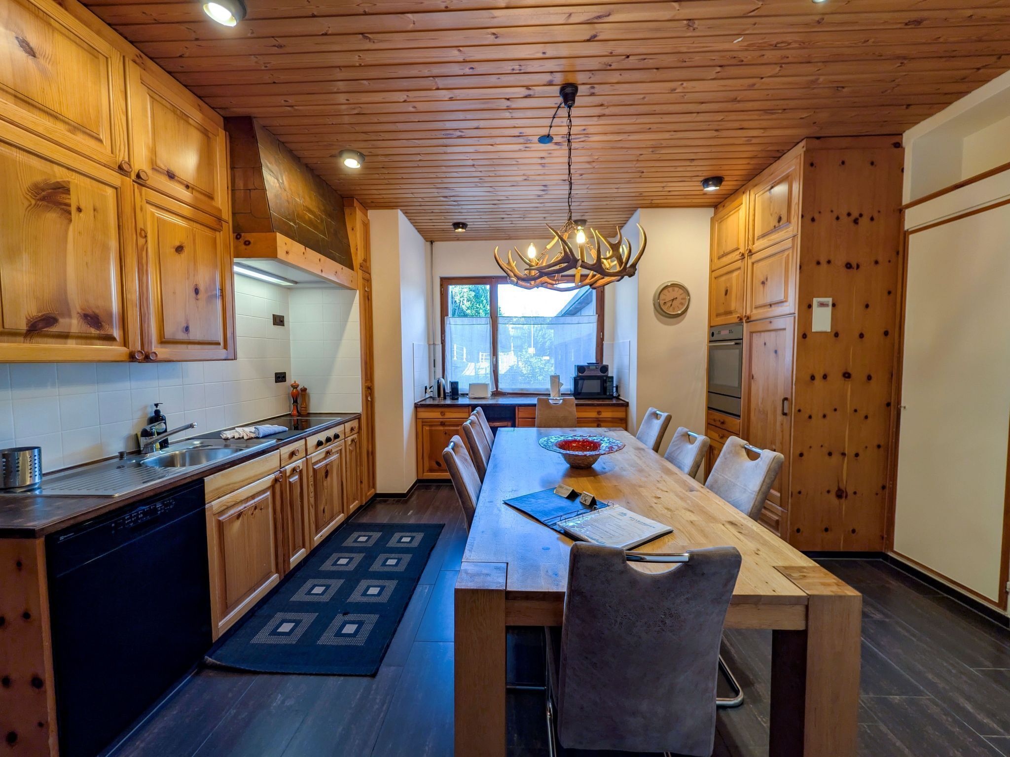 A modern kitchen with wooden cabinets, a dining table, and a chandelier.
