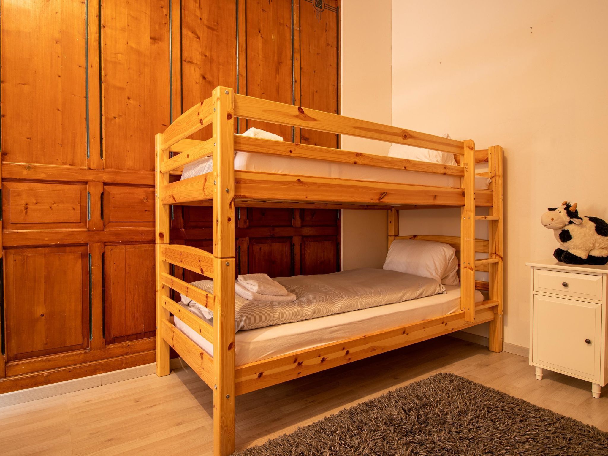 Een stapelbed met houten frame, een klein nachtkastje en een pluche speelgoed aan de rechterkant.