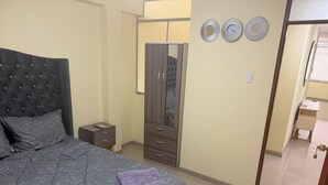 Une chambre à coucher avec un lit, une table de chevet, une armoire et une salle de bain visible à travers une porte ouverte.
