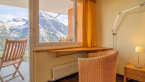 A room with a view of mountains, a wooden chair, a wicker chair, a table, and a lamp. - Casa Linda 8 by Arosa Holiday Appartement/Fewo,  , 7-Bettwohnung Linda 8 by Interhome (Arosa)