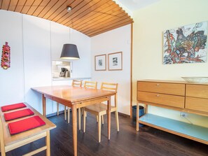 Eine moderne Küche mit Holzausstattung, einem Esstisch mit Stühlen, einer Pendelleuchte und einem Wandbild.