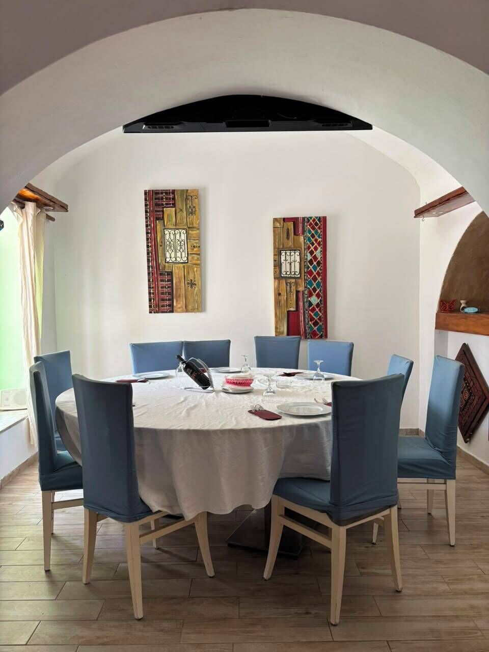 Un comedor con una mesa redonda, sillas azules y dos obras de arte en las paredes.