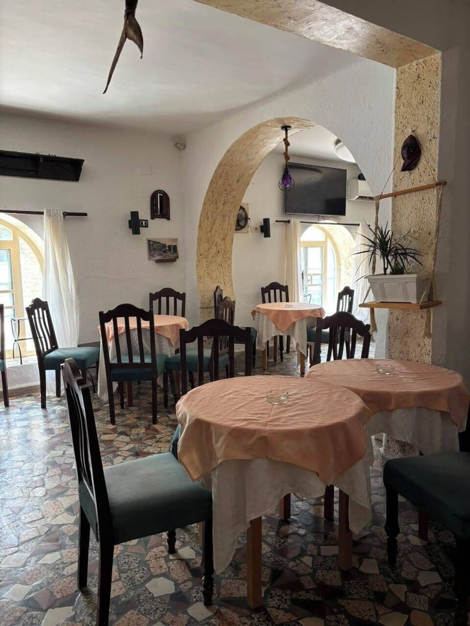 A dining area with round tables, chairs, a tiled floor, and a television on the wall.