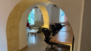 An interior with a wooden table, black chairs, a patterned armchair, and a large arched doorway leading to a balcony.