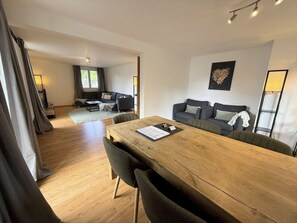 Een moderne woonkamer met een houten eettafel, banken en een groot raam.