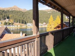 Un balcon en bois offrant une vue sur un lac, une forêt et des montagnes.