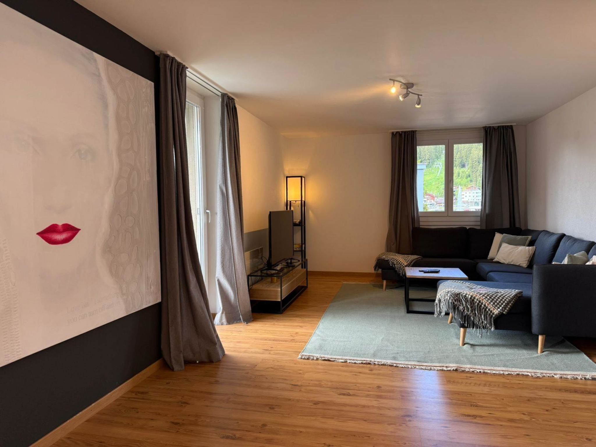 En moderne stue med sofa, sofabord, lampe og udsigt til det frie gennem et vindue.
