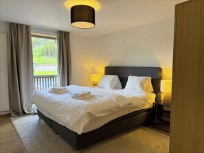 Ein Hotelzimmer mit einem großen Bett, zwei Nachttischlampen, Blick auf Grünflächen und einem Holzschrank.