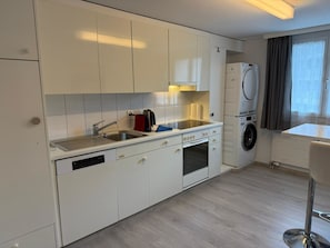 Une cuisine moderne avec des meubles blancs, un lave-vaisselle encastré, une cuisinière et un lave-linge.