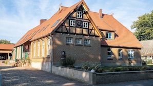 A traditional half-timbered house with a steeply pitched roof, a visible clock, and a small garden area.